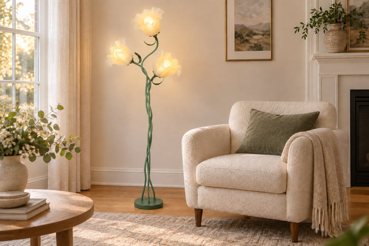 Three-flower sage-green floor lamp beside an ivory accent chair in a warm neutral living room.