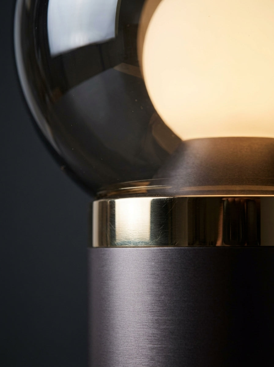 Macro detail of brushed aluminum base, brass accent ring, and smokey crystal glass orb
